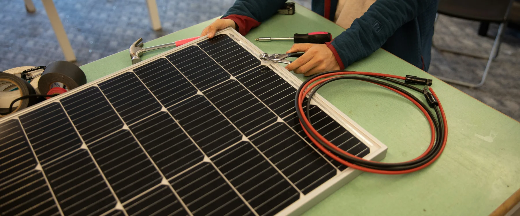 Person working on a solar panel beside coiled red and black PV cables with connectors