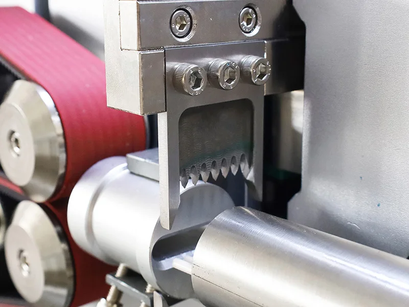 Close-up of a cutting blade, red feed belts and wire guide on a wire-processing machine