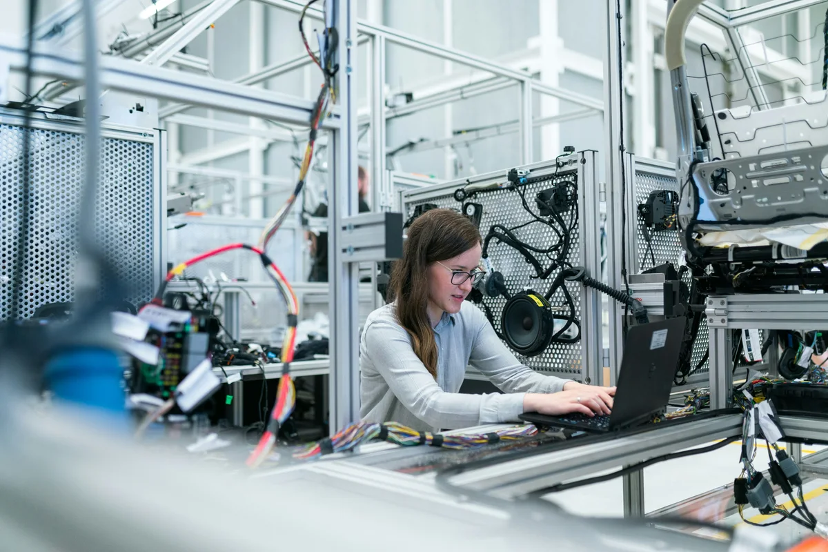 Woman using a laptop at a workstation surrounded by automotive wiring harnesses