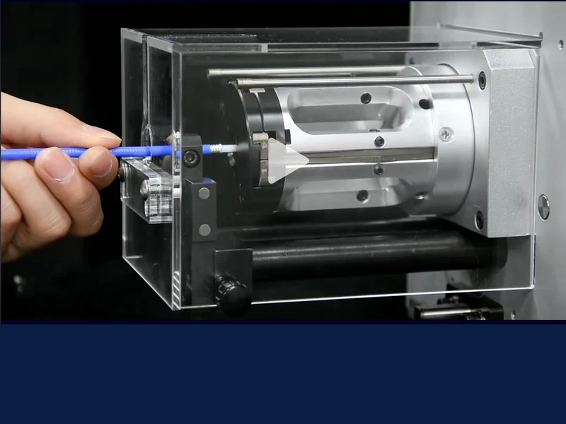 Paused video showing a hand holding blue cable at a wire-stripping mechanism behind a clear guard